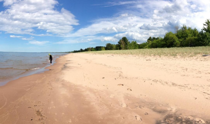 A beach next to Lake Superior on a sunny day. In the distance, a person is wading in the water.
