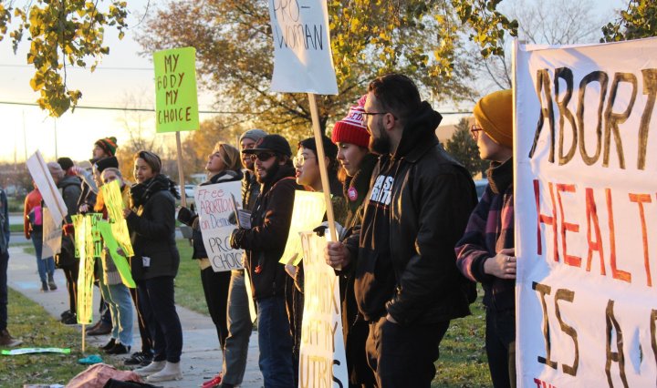 A picture of people standing in a line, holding signs in support of abortion rights, while the sun sets.